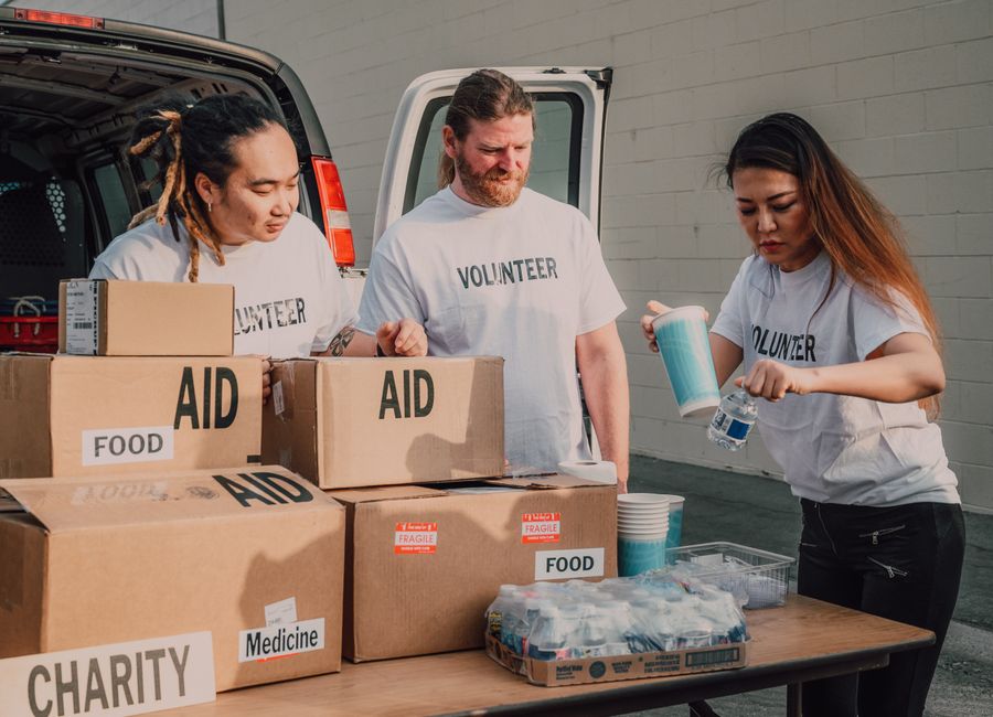 A diverse group of community volunteers work together around a table in a bright community center, representing an organized local response network after a disaster.