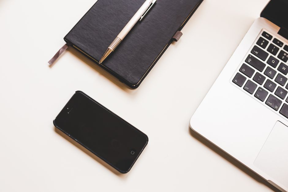 A person thoughtfully makes notes in a journal while working on a laptop at a clean, organized desk, representing the careful decision-making process for enrolling in a school.