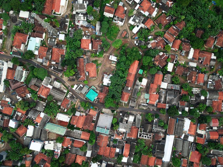 An aerial drone shot looking down on a dense grid of city rooftops and streets, illustrating the vast scale of urban housing and the challenge of municipal regulation.
